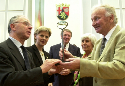 Foto: Präsident Franz verleiht die Skulptur, die zur Auszeichnung gehört, an Professor Behnisch. Drei Menschen stehen im Hintergrund und sehen zu.
